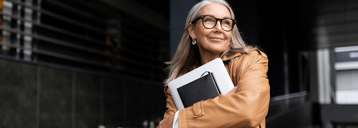 Een dame met bril staat buiten kantoor met een laptop in haar handen