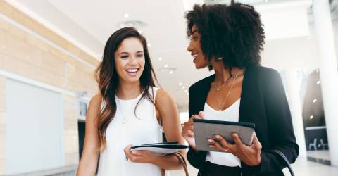 2 blijde jonge vrouwen lopen door het kantoor heen en hebben een overleg